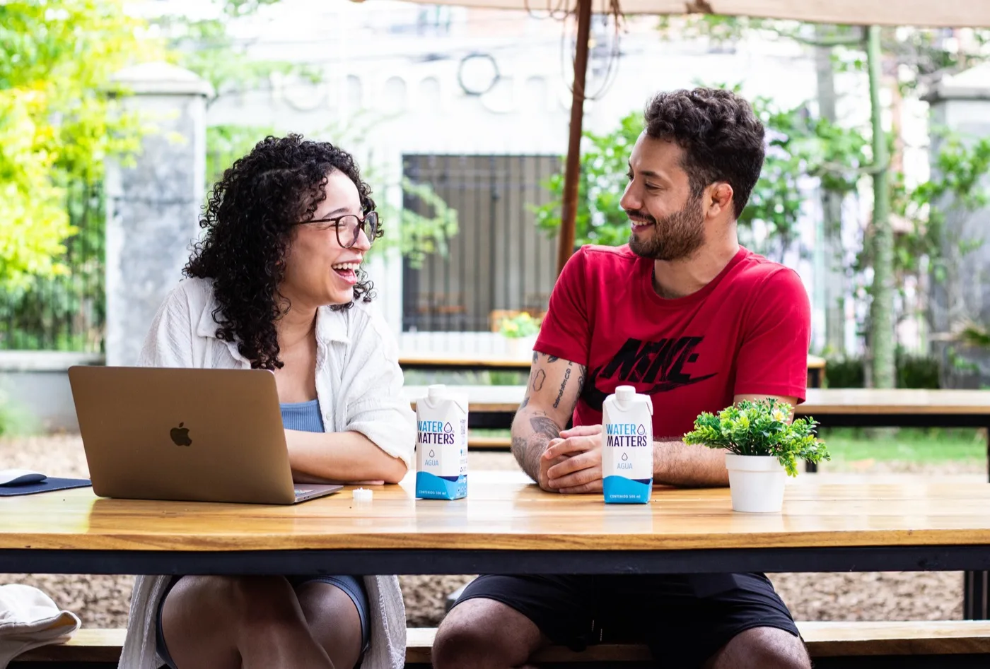 Dos personas trabajando en una mesa al aire libre, con dos envases de Water Matters